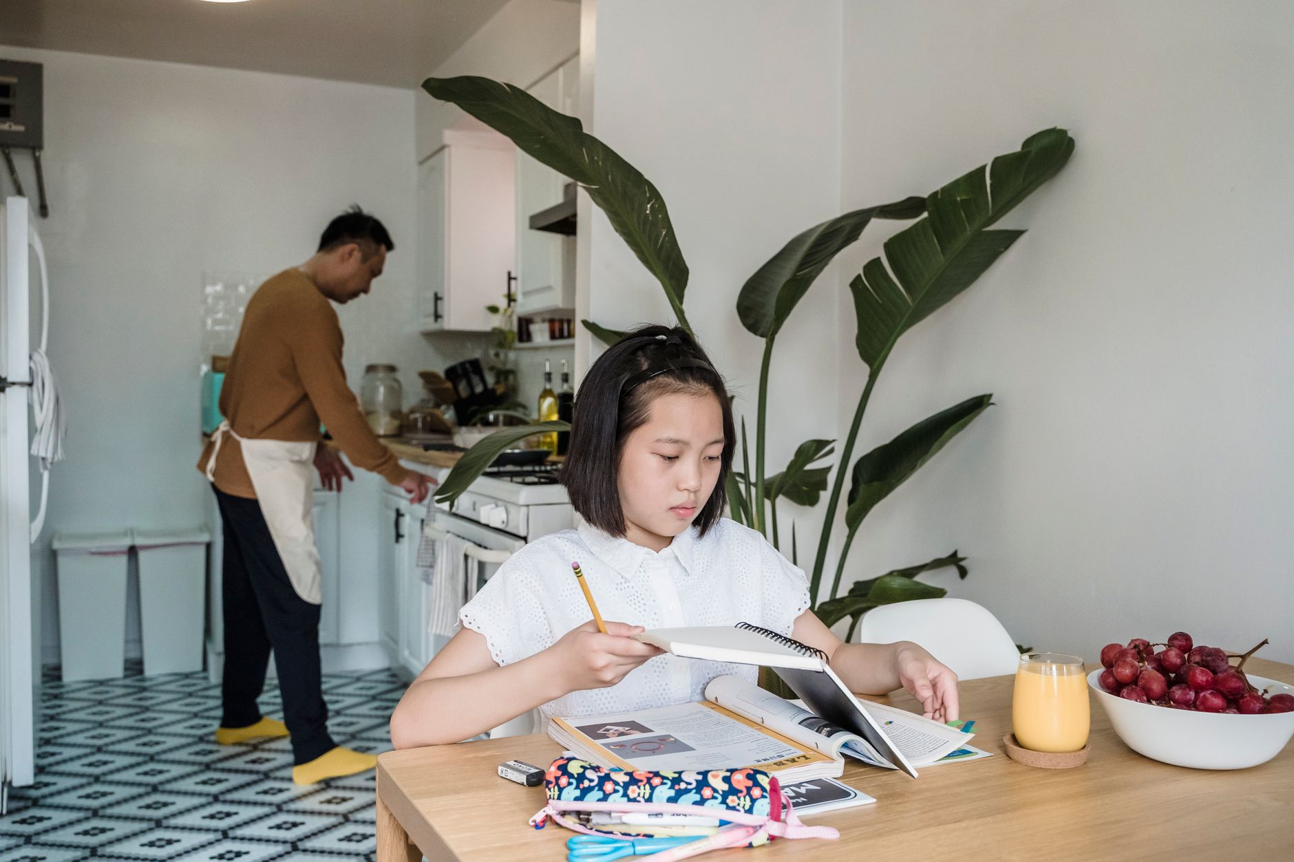 A child focuses on homework at the dining table with a parent cooking in the kitchen — illustrating: How to choose a VPN for your kids without getting lost in tech jargon
